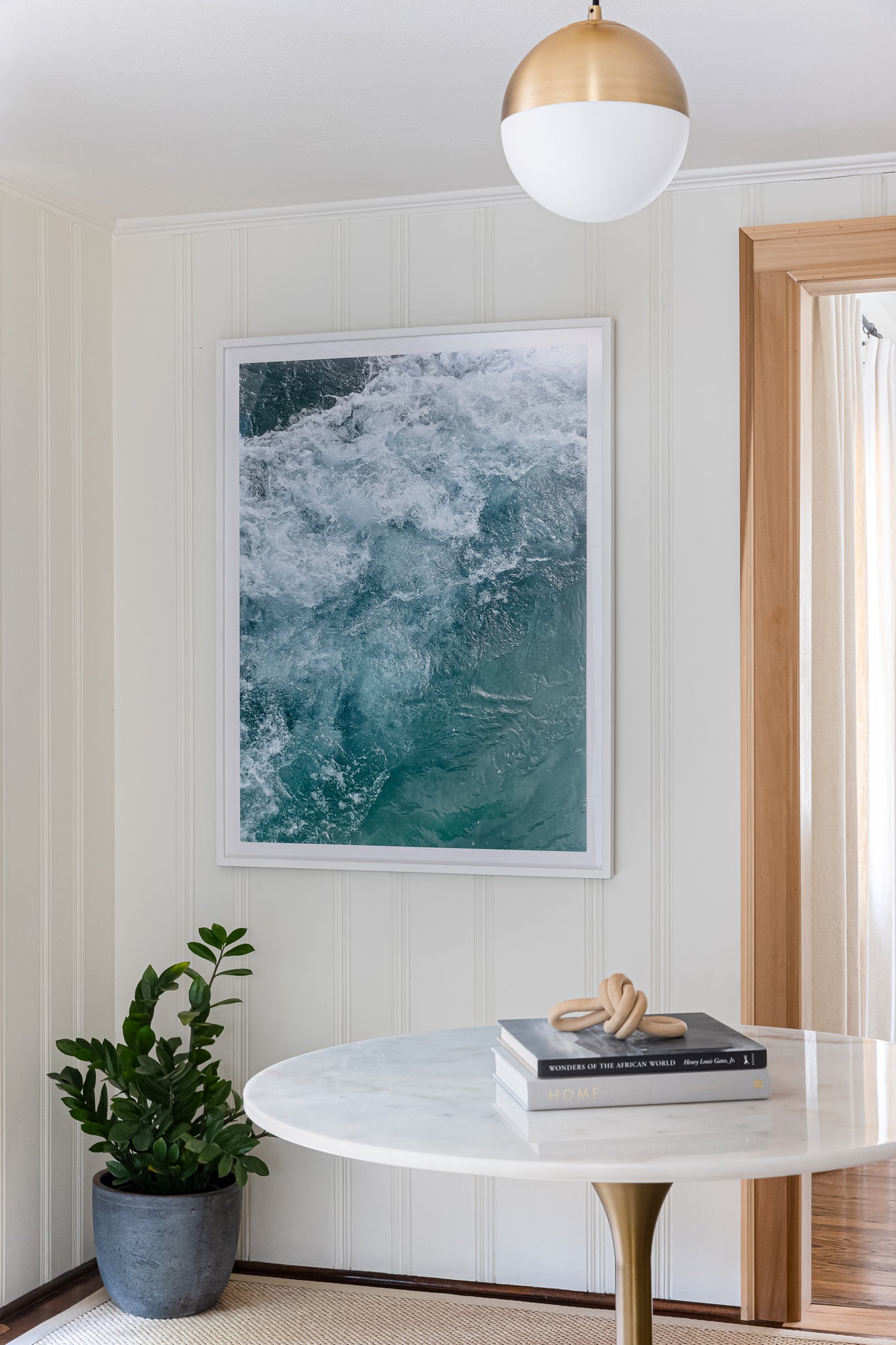 Wave framed print hanging on shiplap wall with plant, table, books, and hanging light pendant