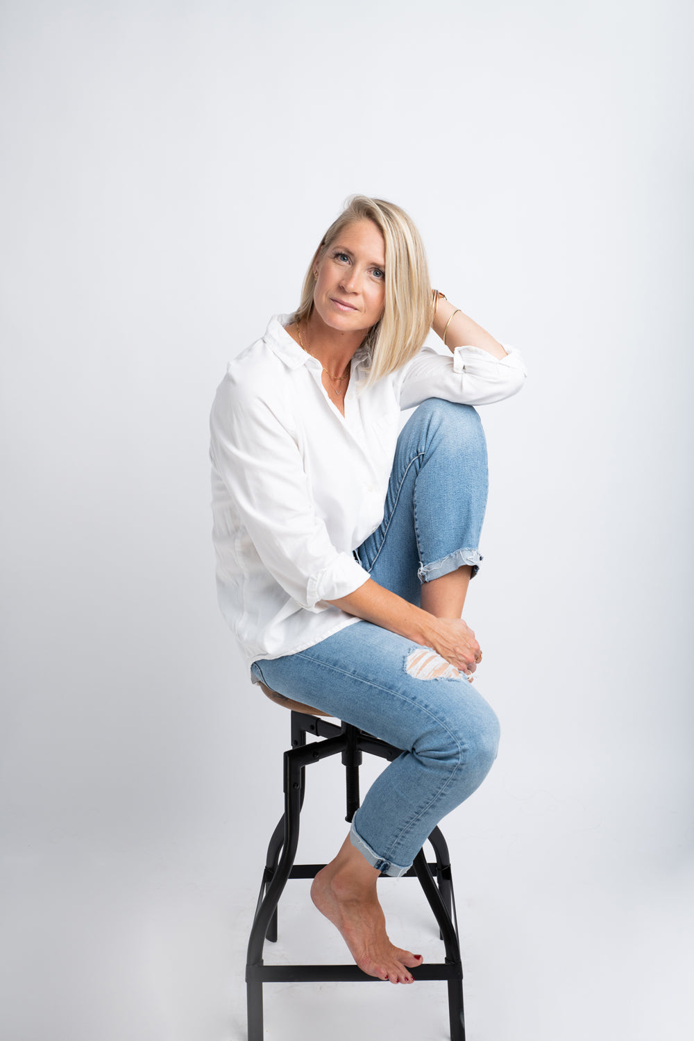 Headshot of photographer Amanda Anderson sitting on a stool in jeans and white shirt